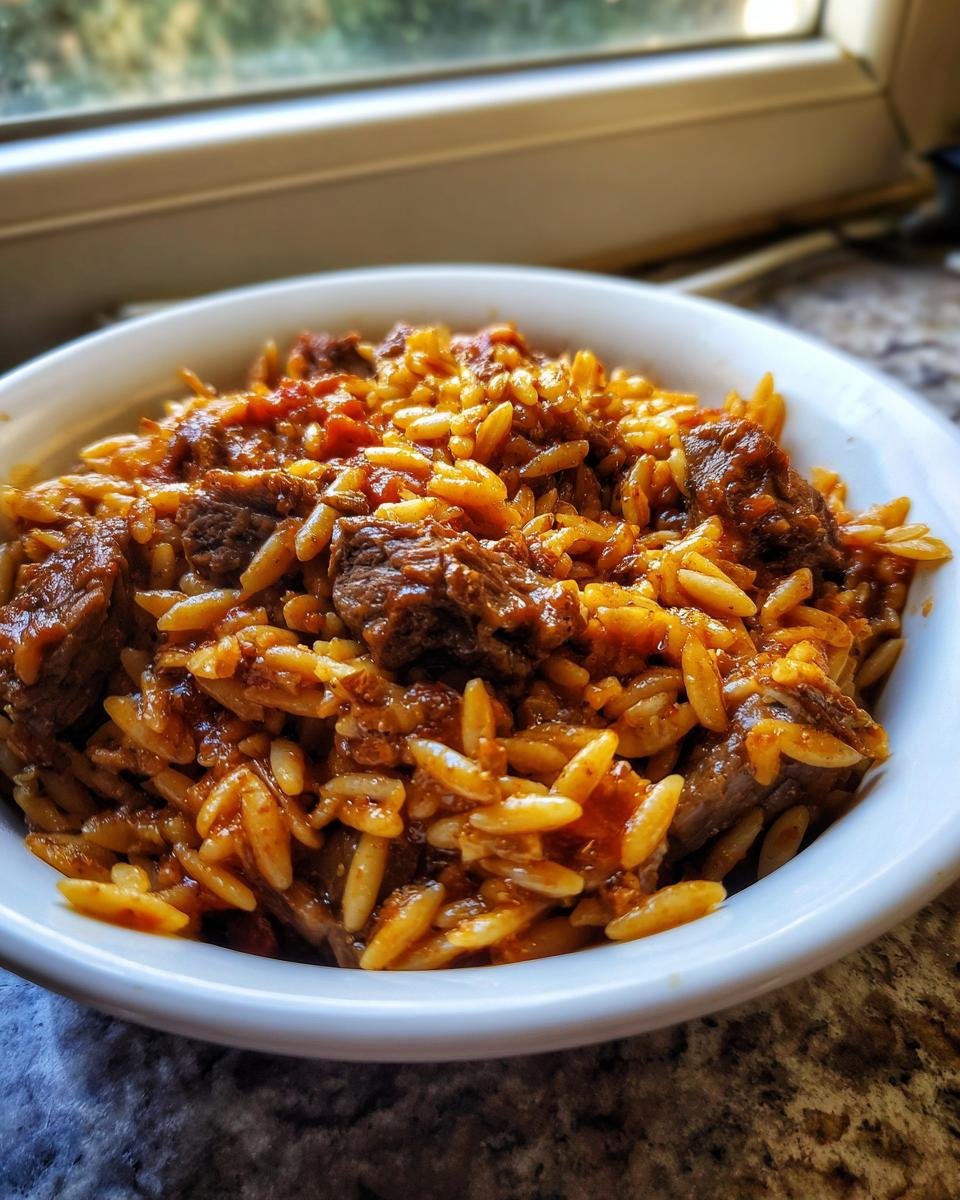 Close-up of a white bowl filled with rich, tomato-sauced Beef Giouvetsi, featuring tender beef chunks and orzo pasta.