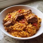 Close-up of a white bowl filled with rich Beef Giouvetsi, featuring tender beef chunks mixed with tomato-sauced orzo pasta.