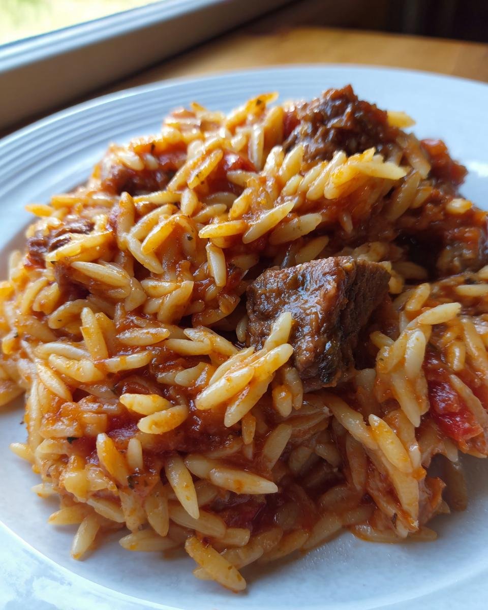 A close-up serving of Beef Giouvetsi featuring tender beef chunks mixed with orzo pasta coated in a rich tomato sauce.