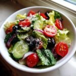 A close-up of a vibrant Big Classic Italian Salad featuring lettuce, cherry tomatoes, cucumbers, black olives, red onion, and grated cheese.