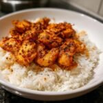 Close-up of seasoned Cajun Chicken And Rice served in a white bowl, showing bright orange chicken pieces over white rice.