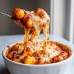 A spoonful of cheesy Gnocchi And Tomato Bake showing incredible cheese pull over a white bowl.