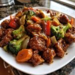 A close-up of a plate filled with glossy Chicken And Veggie Stir Fry featuring coated chicken pieces, broccoli, carrots, and onions.
