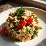 A mound of vibrant Chicken Couscous Salad topped with shredded chicken, diced cucumber, and red pepper.