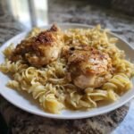 Two golden-brown chicken thighs served over a bed of buttery egg noodles, the main dish for Chicken With Buttered Noodles.