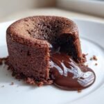 Close-up of a freshly baked Chocolate Lava Cake with its molten center oozing out onto a white plate.