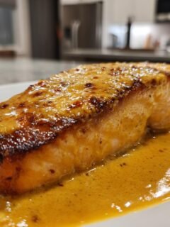 A perfectly cooked fillet of Coconut Curry Salmon With Garlic Butter resting in a pool of rich, yellow sauce.