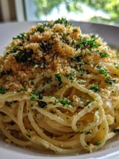 A close-up shot of creamy Garlic Bread Pasta topped generously with toasted breadcrumbs and fresh parsley.