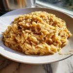 A close-up serving of rich, creamy Garlic Parmesan Orzo pasta on a white plate, glistening in natural light.