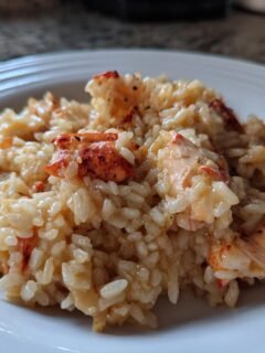 Close-up of a serving of rich, Creamy Lobster Risotto studded with chunks of bright red lobster meat on a white plate.