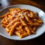 Close-up of penne pasta coated in a rich, creamy Roasted Red Pepper Pasta sauce, topped with grated Parmesan cheese.