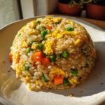 A dome-shaped serving of vibrant Egg Fried Rice, featuring scrambled egg, bright green peas, and diced carrots, sprinkled with sesame seeds.