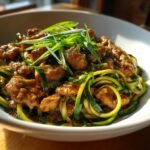 A bowl of Garlic Chicken Zucchini Noodles Stir Fry topped with fresh green onions.