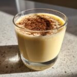 Close-up of a glass filled with creamy Homemade Eggnog Recipe, dusted generously with cinnamon.