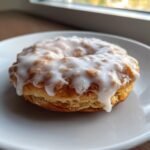 Close-up of a flaky, ring-shaped pastry topped with thick white glaze, resembling a donut, related to Brown Sugar Pop Tart Cookies.