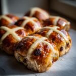 A close-up of freshly baked, glazed Hot Cross Buns With Candied Fruit, featuring distinct white crosses.