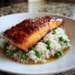 Close-up of a perfectly cooked fillet of glazed salmon resting on a bed of white rice and green peas, part of the One Pot Salmon And Rice dish.