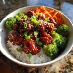 Close-up of a Gochujang Chicken Bowl featuring sticky, glazed chicken over white rice with steamed broccoli and shredded carrots.