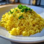 A mound of fluffy, vibrant yellow Greek Lemon Rice garnished with fresh chopped parsley on a white plate.