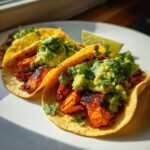 Three delicious Grilled Salmon Tacos topped with chunky avocado salsa and fresh cilantro, served with a lime wedge.