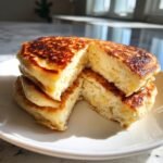 Close-up of a stack of fluffy High Protein Cottage Cheese Pancakes cut in half, showing the airy interior texture.