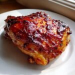 Close-up of a perfectly cooked Honey Chipotle Chicken thigh with a thick, glossy, caramelized glaze.