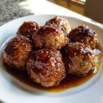 Close-up of six glistening Honey Garlic Turkey Meatballs coated in a thick, dark glaze, resting in sauce on a white plate.