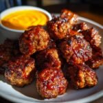 Close-up of glazed Korean Bbq Meatballs piled on a white plate next to a small bowl of bright orange spicy mayo dip.
