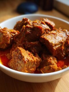 Close-up of tender chunks of Lamb Madras Curry coated in a thick, vibrant red-orange sauce, served in a white bowl.