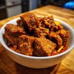 Close-up of tender chunks of Lamb Madras Curry coated in a thick, rich, reddish-brown spice paste served in a white bowl.