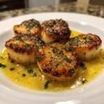 Five perfectly seared Lemon Butter Scallops resting in a pool of glistening lemon butter sauce, garnished with parsley.