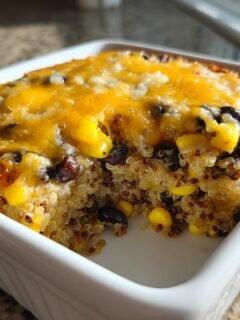 A close-up view of a serving of Mexican Quinoa Casserole topped with melted cheddar cheese, corn, and black beans.