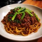 Close-up of rich Mongolian Ground Beef Noodles topped with thick, savory sauce and bright green scallions.