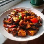 Close-up of a plate featuring a rich Mushroom And Tofu Stir Fry with chunks of tofu, mushrooms, and colorful bell peppers.