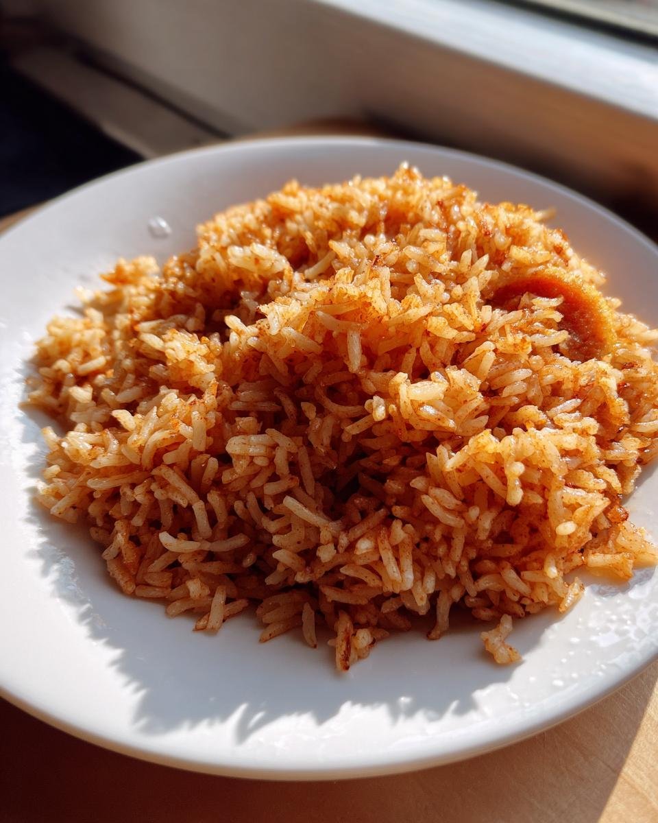 A mound of fluffy, reddish-orange Persian Tomato Rice served on a white plate, highlighted by natural sunlight.