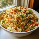 A large white bowl filled with Ramen Noodle Salad With Cabbage, topped generously with sliced almonds and green onions.