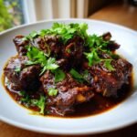 Close-up of rich, dark brown Lamb Kalya pieces swimming in gravy and topped with fresh cilantro.