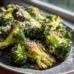 Close-up of roasted Garlic Parmesan Broccoli florets, topped with grated cheese, served on a grey plate.