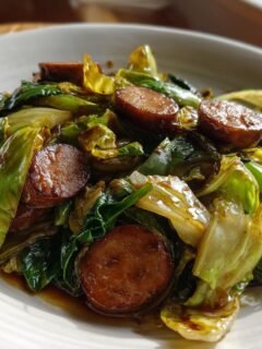 A close-up view of a serving of Sausage And Cabbage Stir Fry, featuring browned sausage slices mixed with wilted green cabbage.