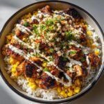 A close-up overhead view of a Street Corn Chicken Rice Bowl featuring charred chicken, white rice, corn, cotija cheese, and crema drizzle.