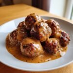 A close-up of several perfectly browned Swedish meatballs smothered in creamy brown gravy on a white plate.