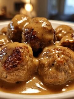 A close-up shot of several perfectly browned Swedish meatballs swimming in rich, creamy gravy.