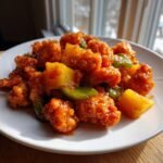 A close-up of crispy Sweet And Sour Chicken With Pineapple chunks coated in a vibrant orange sauce.