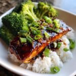 Close-up of a Teriyaki Salmon Bowl featuring a glazed salmon fillet over white rice with steamed broccoli and green onions.