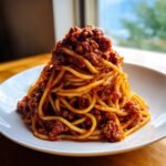 A tall mound of spaghetti noodles generously topped with rich Turkey Bolognese Spaghetti sauce on a white plate.