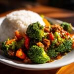 Close-up of vibrant Vegetable Stir Fry With Peanut Sauce featuring broccoli and peppers, served next to a mound of white rice.
