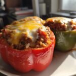 Two baked Vegetarian Stuffed Bell Peppers With Rice, one red and one green, topped with melted cheese.