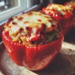 Close-up of a bright red bell pepper stuffed with rice and topped with melted, browned mozzarella cheese.
